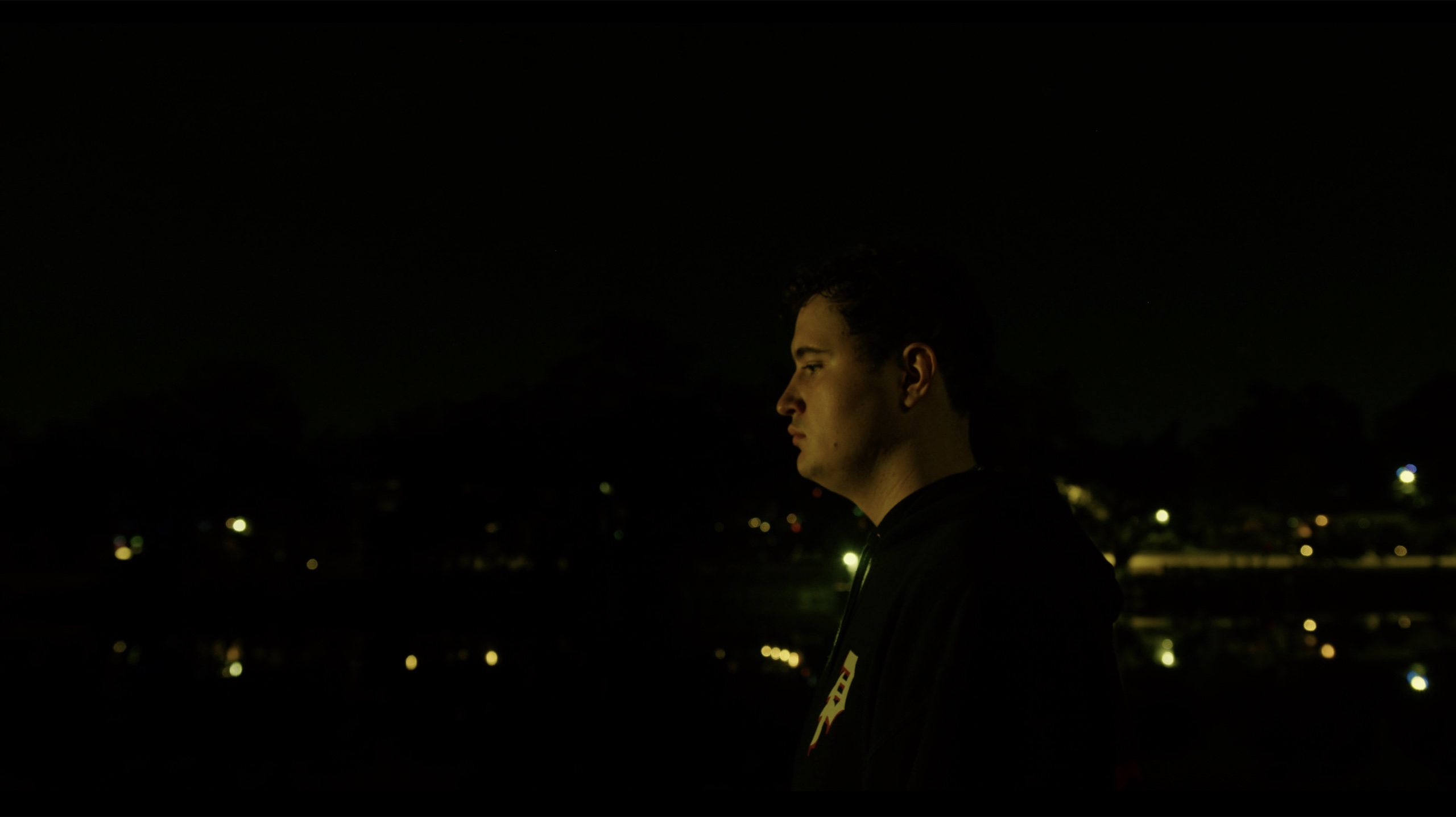A man in profile against distant lights at night.