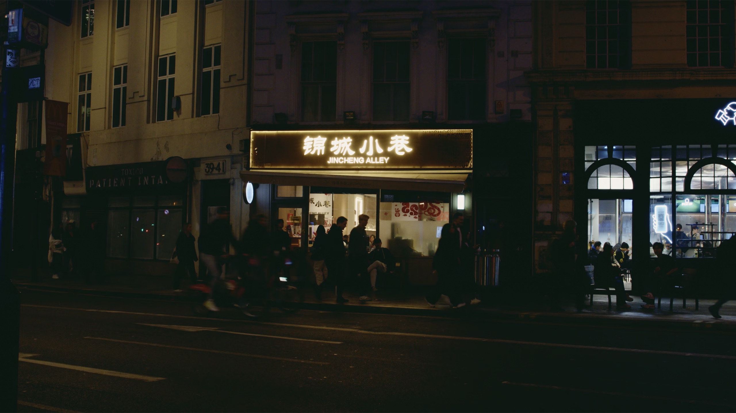 People passing the illuminated Jincheng Alley storefront at night.