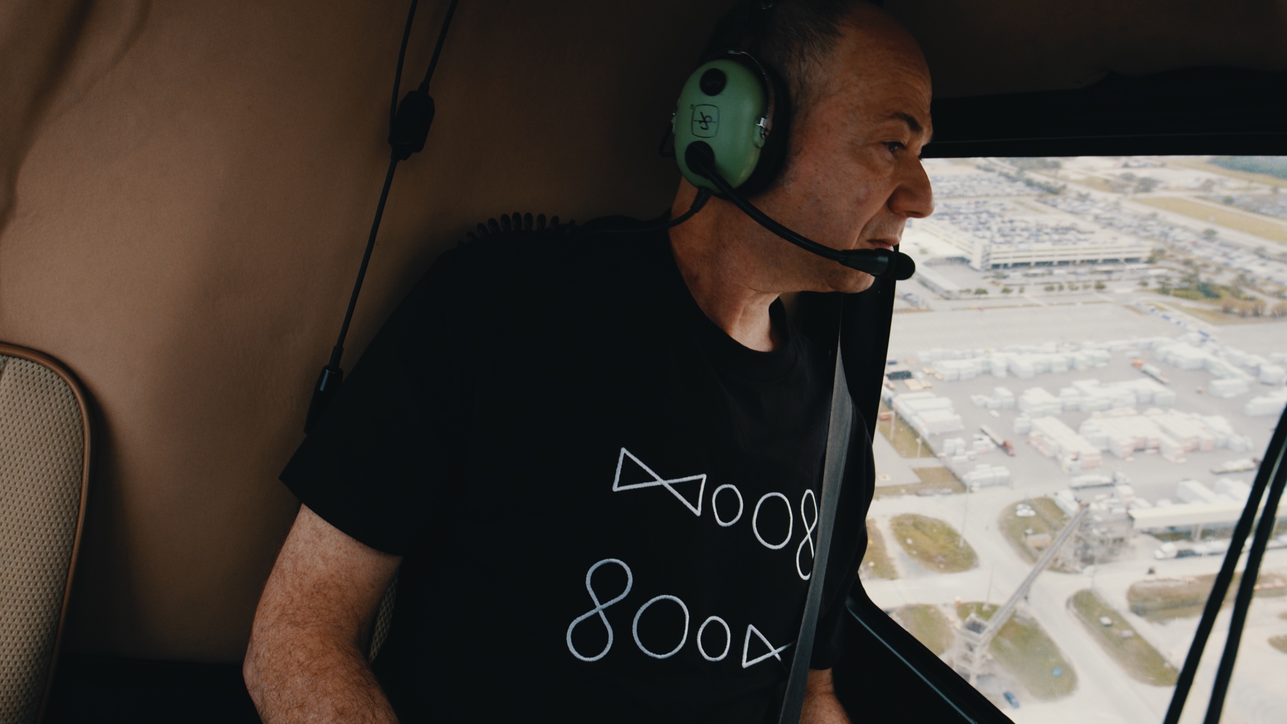 A man wearing a green aviation headset inside a helicopter.